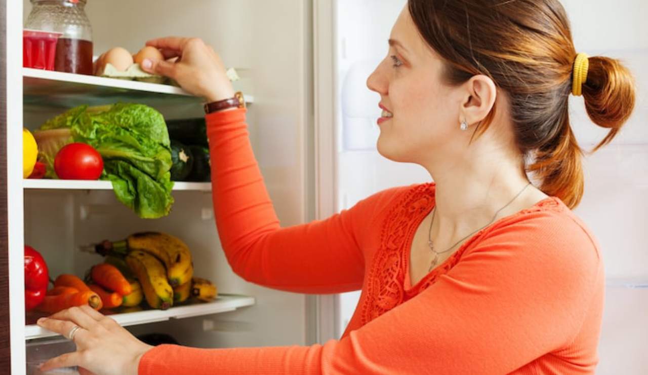 Donna che mette la frutta in frigo